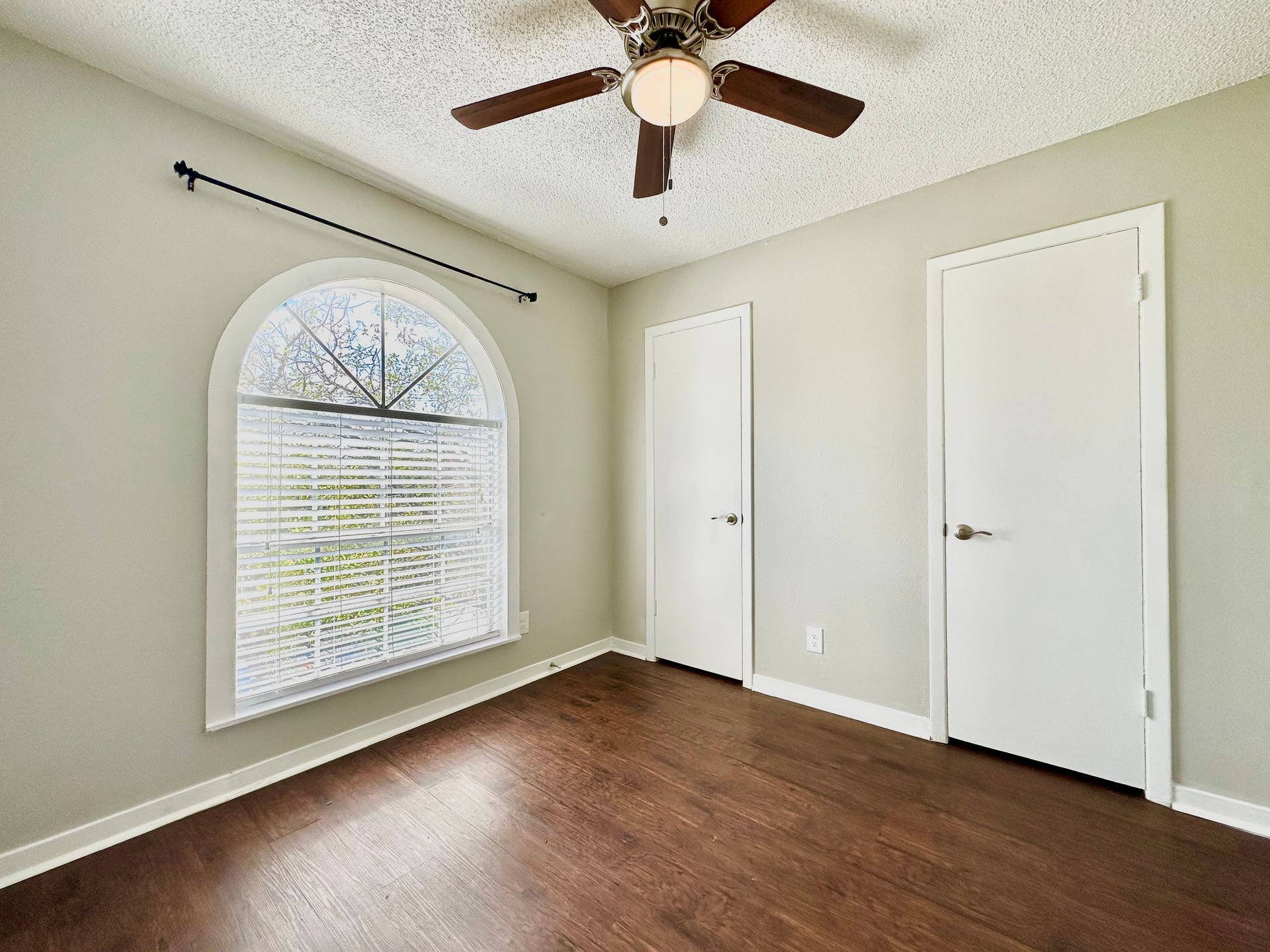 An empty bedroom with a ceiling fan and a large window.