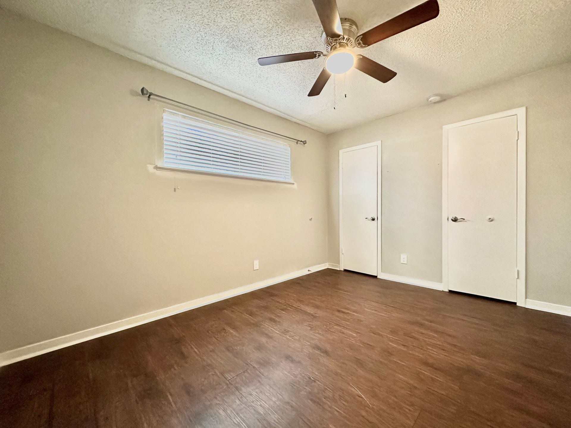 An empty bedroom with hardwood floors and a ceiling fan.