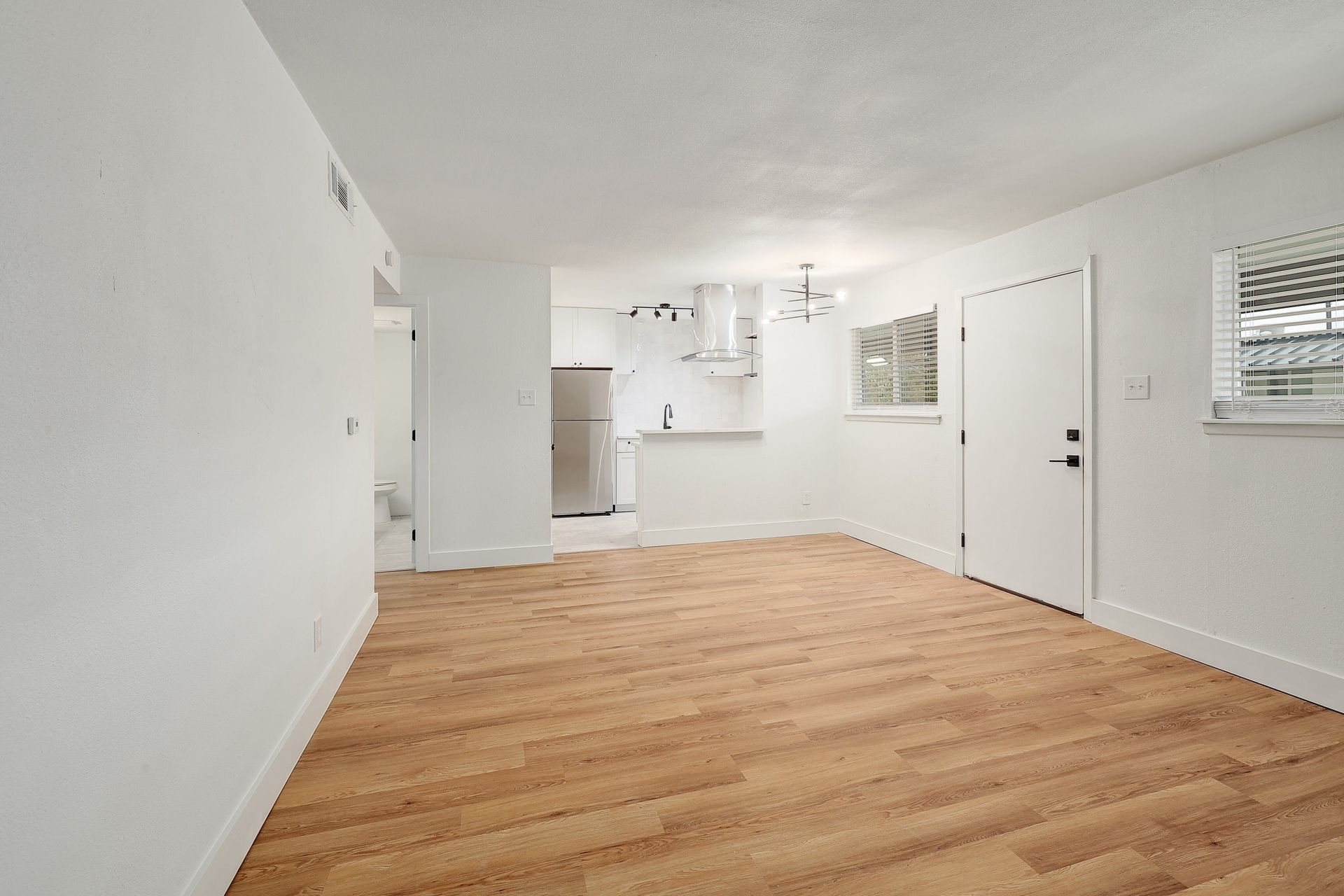 An empty living room with hardwood floors and white walls.