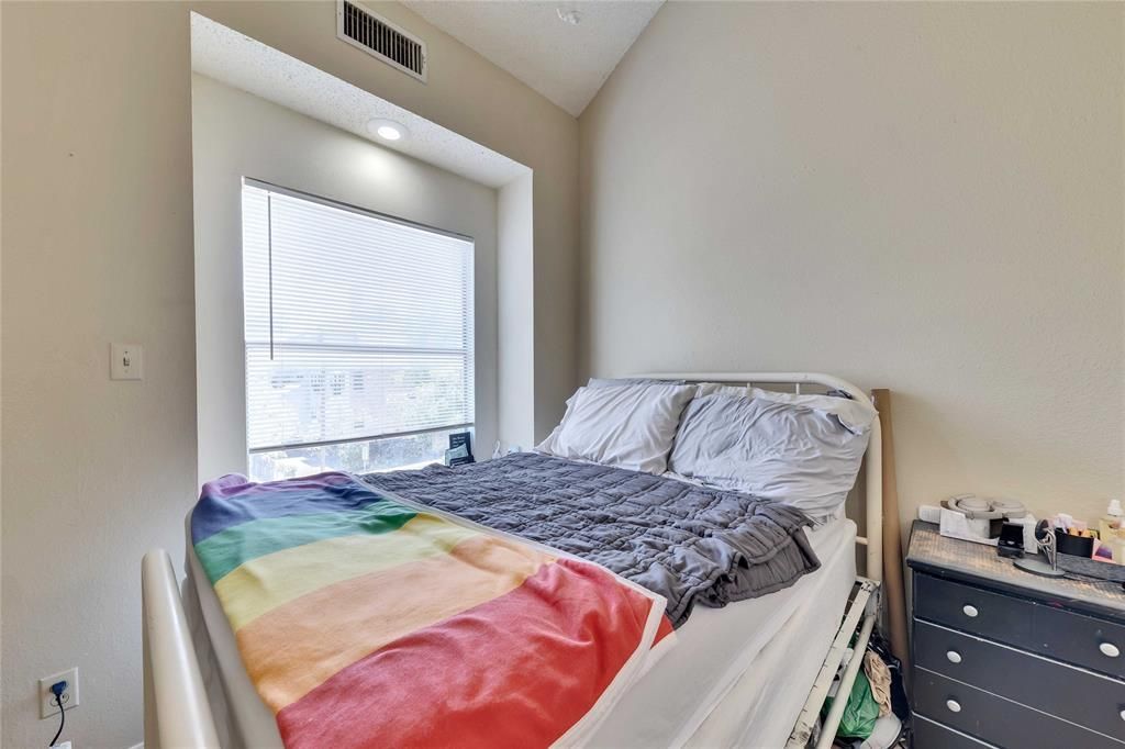 A bedroom with a bed and a window with a rainbow blanket on it.