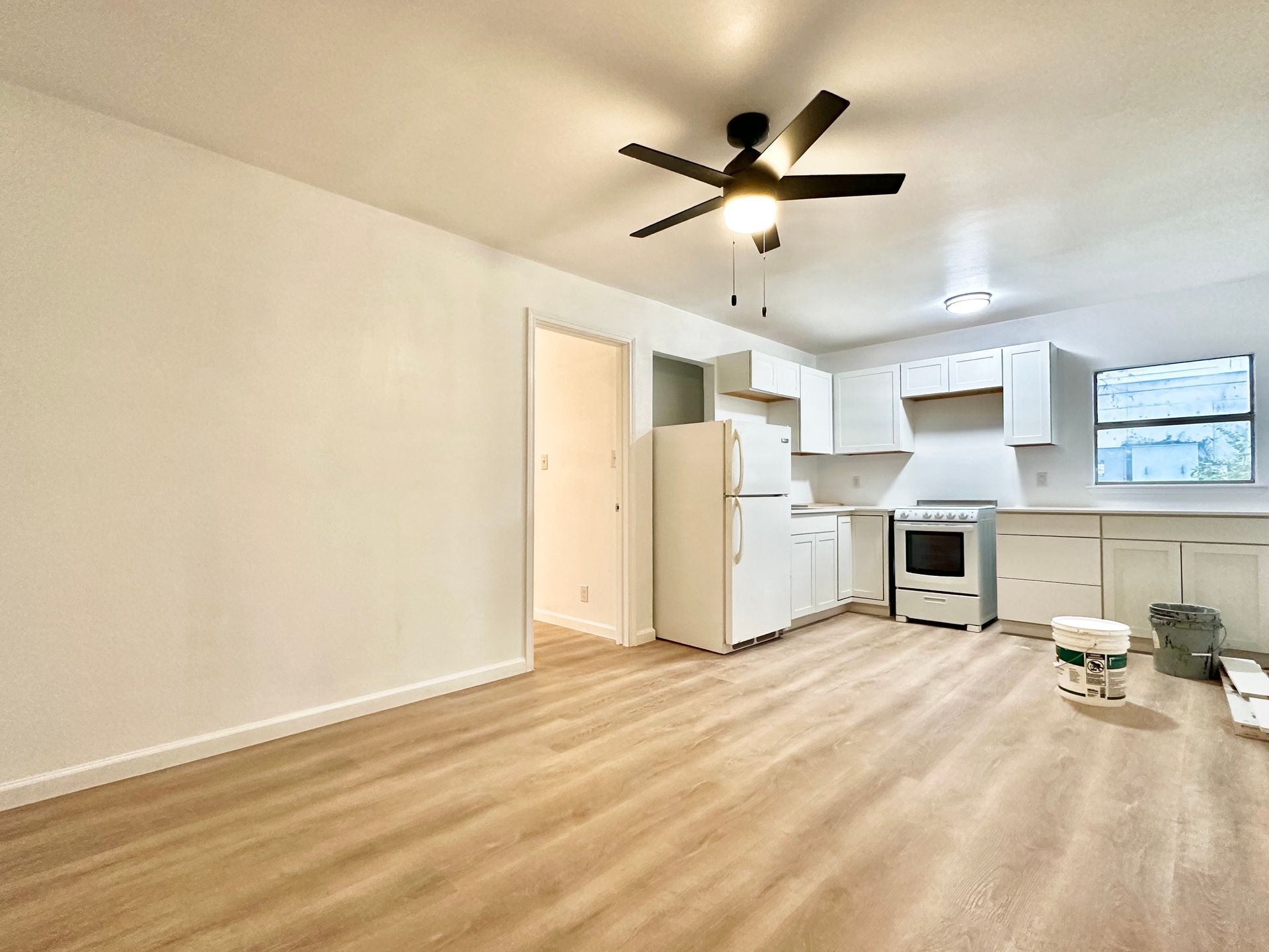 A living room with a ceiling fan and a kitchen in the background.