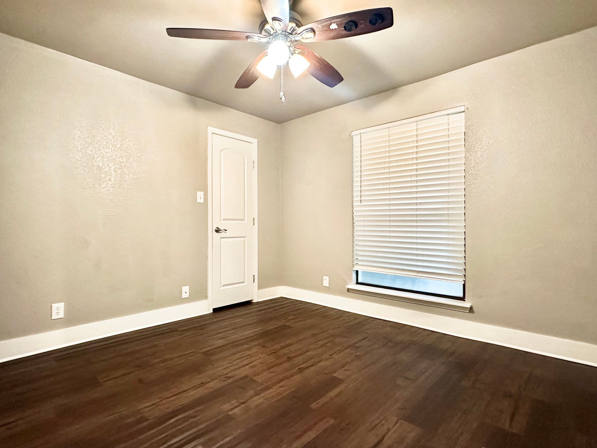 An empty bedroom with hardwood floors and a ceiling fan.