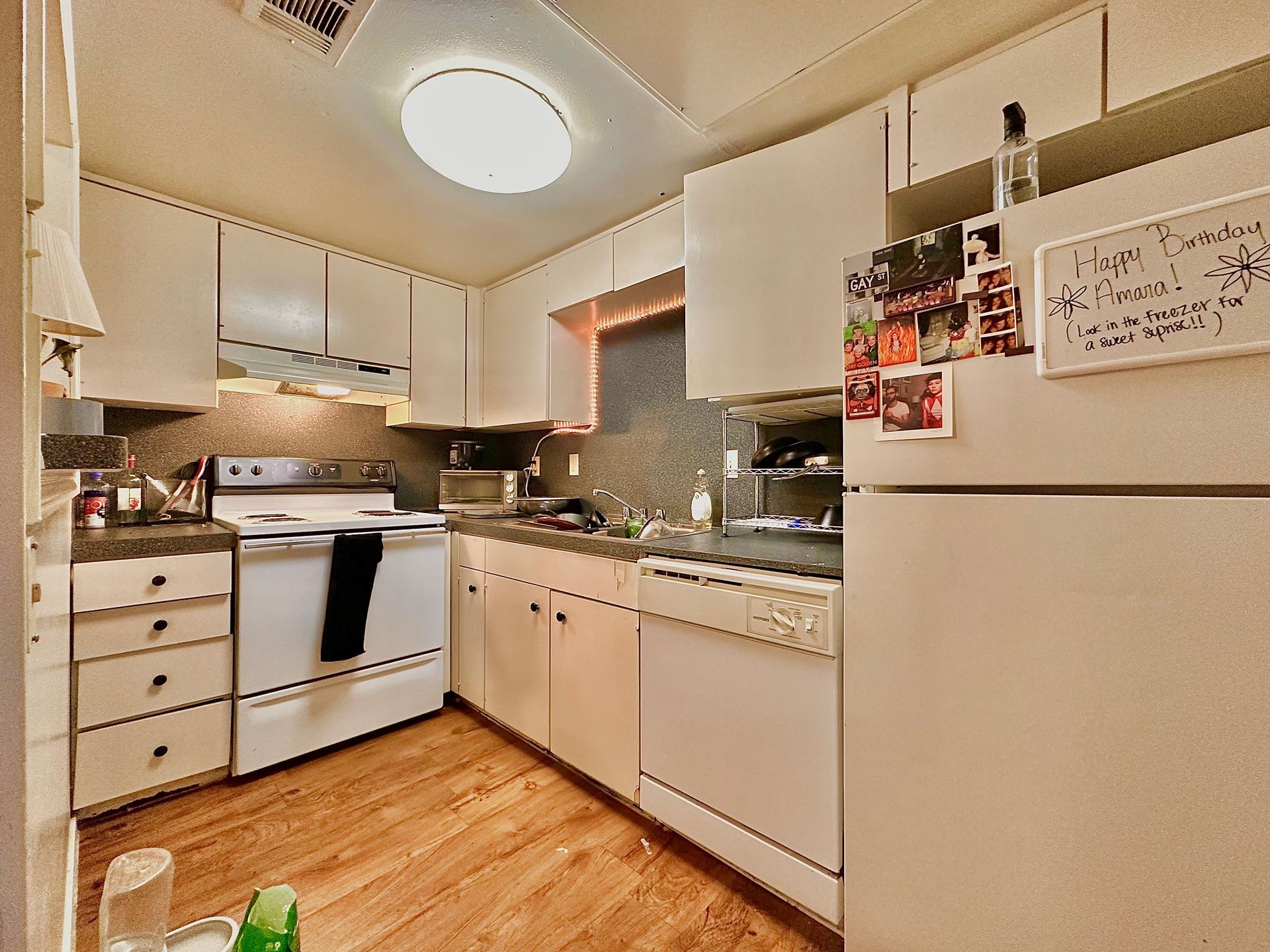 A kitchen with white cabinets , a stove , a refrigerator and a dishwasher.