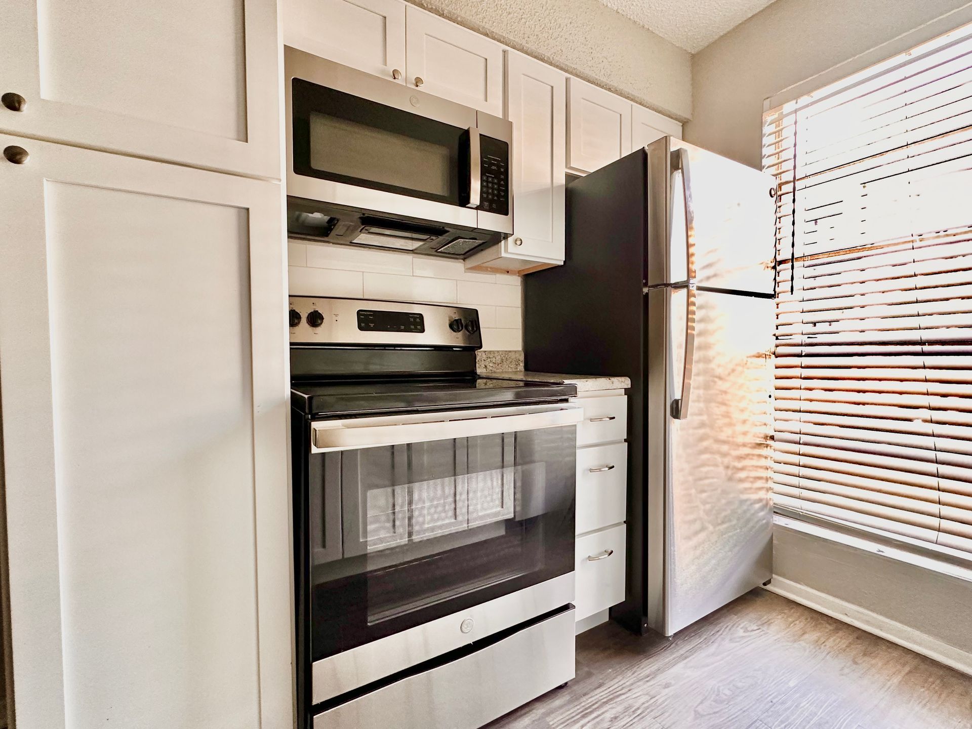 A kitchen with a stove , microwave , refrigerator and white cabinets.