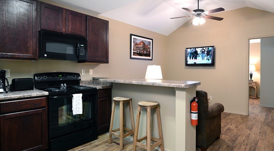 A kitchen with a stove , microwave , stools and a ceiling fan.