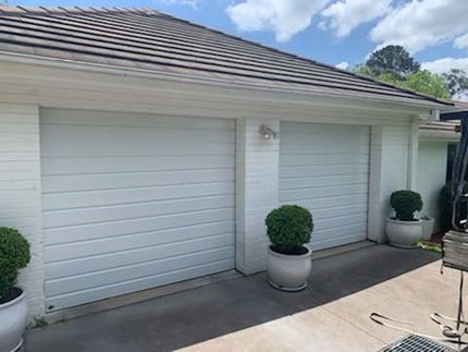 A White Garage Door With Potted Plants in Front of It — Schofield's Garage Doors in Robertson, NSW