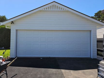 A White Garage With a Black Wheelbarrow in Front of It — Schofield's Garage Doors in Robertson, NSW