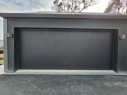 A Black Garage Door is Sitting on the Side of a Road — Schofield's Garage Doors in Robertson, NSW