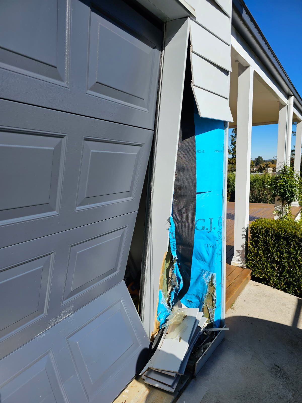 A Broken Garage Door is Sitting on the Side of a House — Schofield's Garage Doors in Robertson, NSW