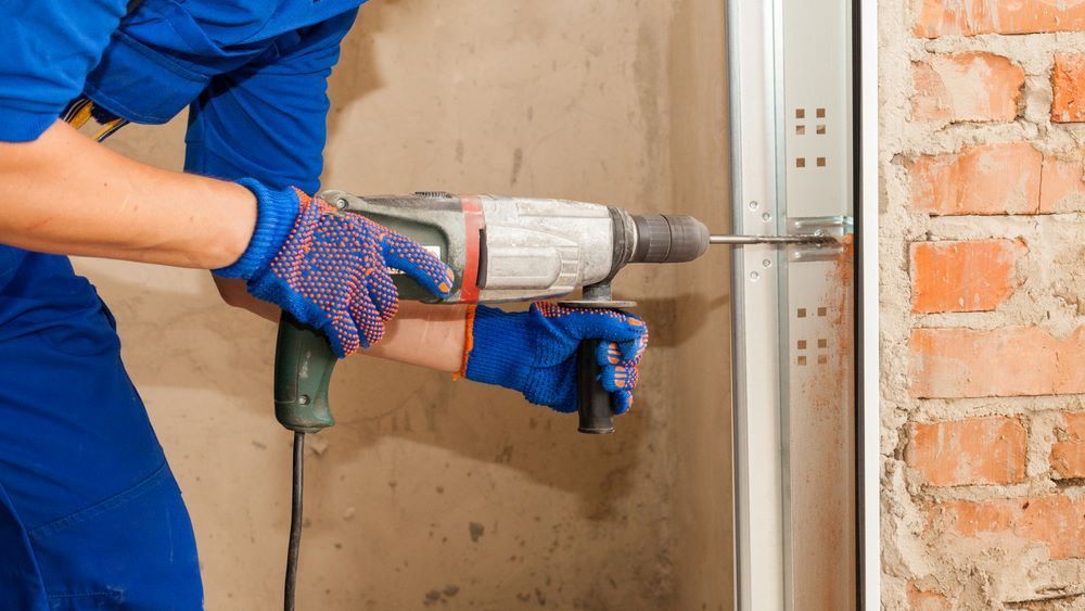 A Man is Using a Drill to Install a Garage Door — Schofield's Garage Doors in Robertson, NSW