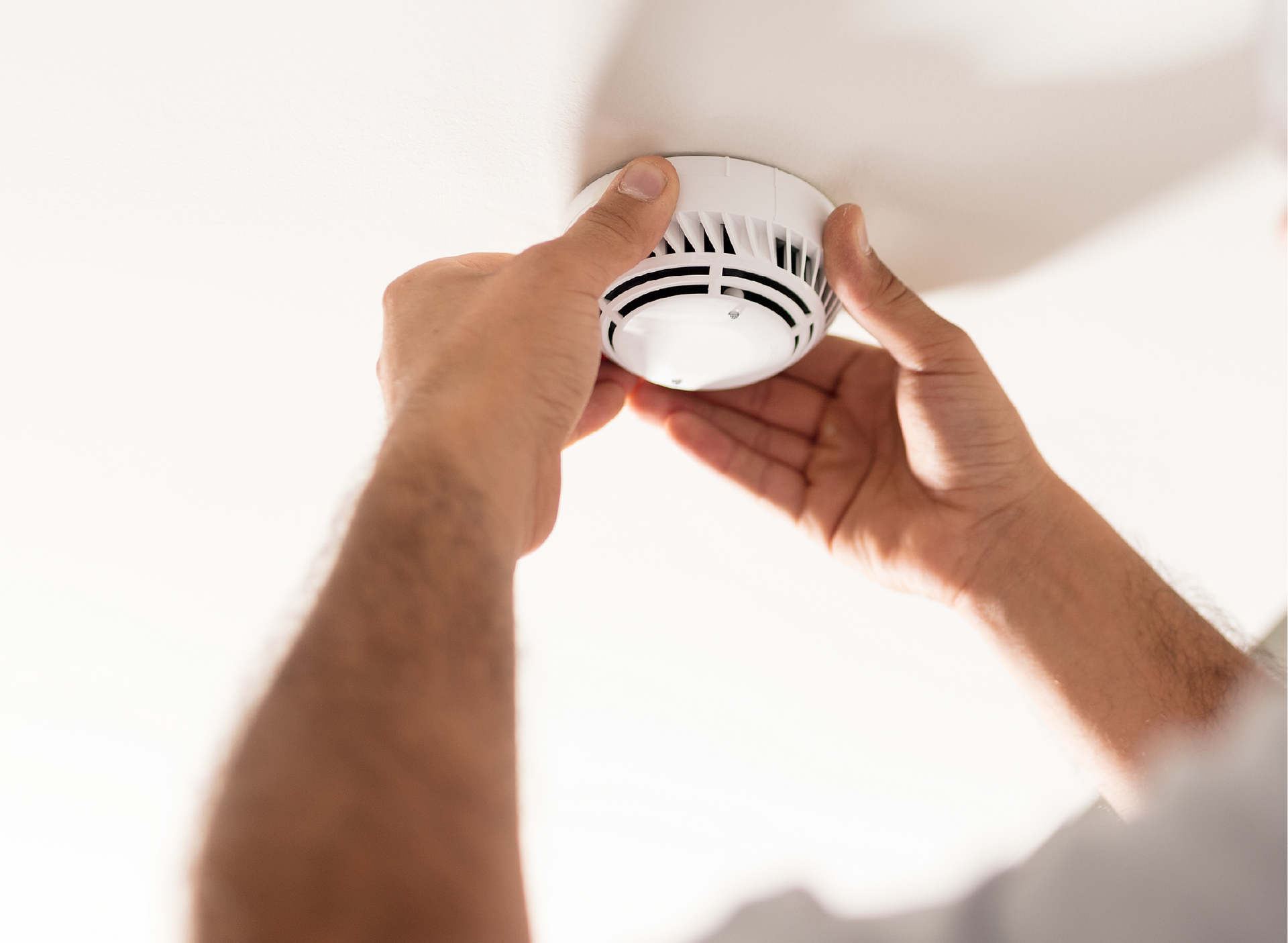 A man is installing a smoke detector on the ceiling.