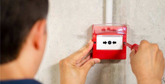 A man is installing a fire alarm on a wall.