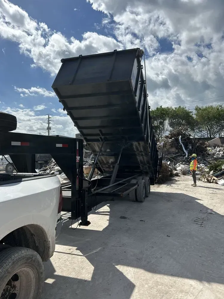 A truck with a black dump trailer tilted upward in an outdoor industrial lot, with a worker standing nearby.