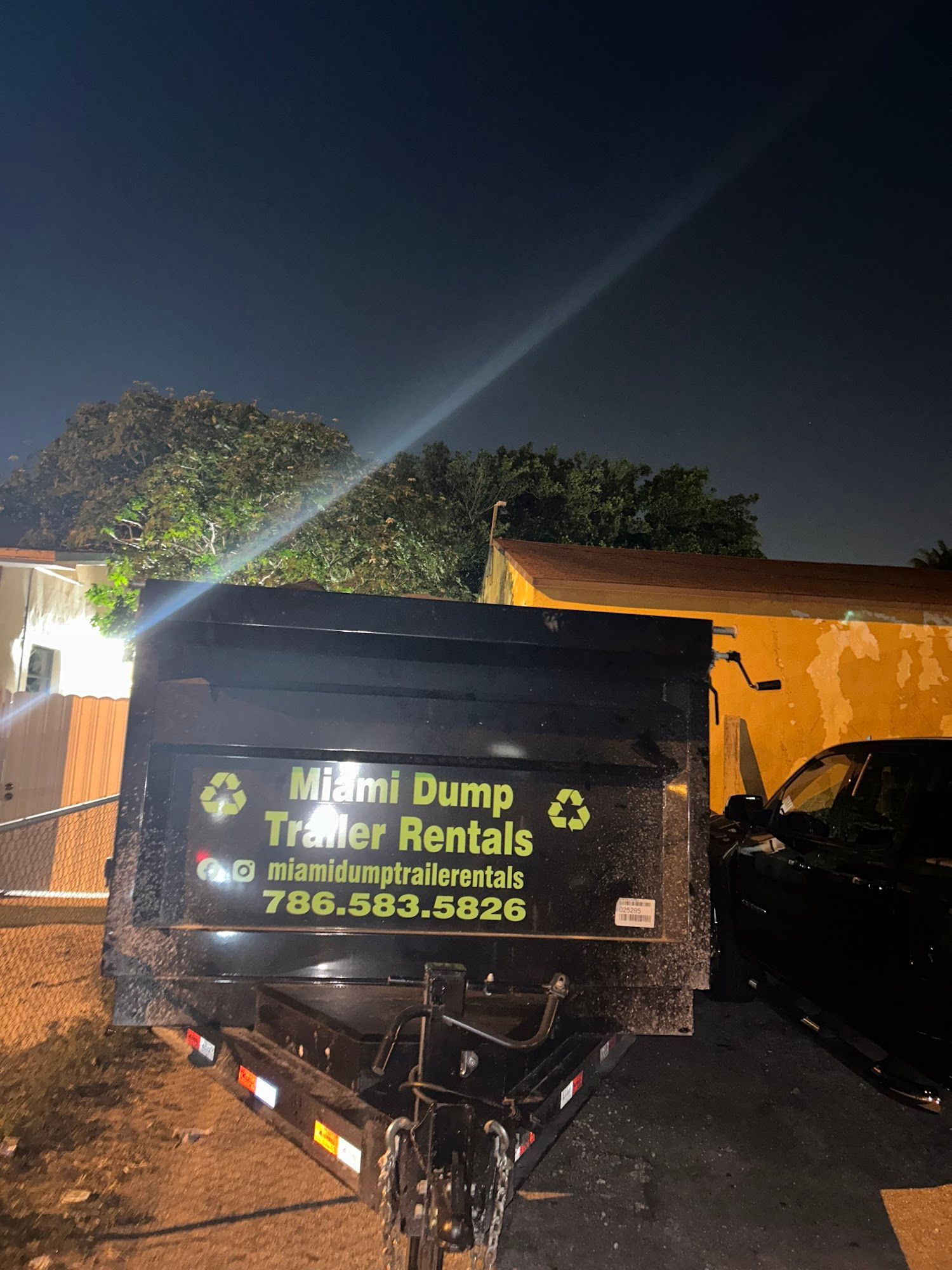 A black dump trailer parked at night features the white and green text 