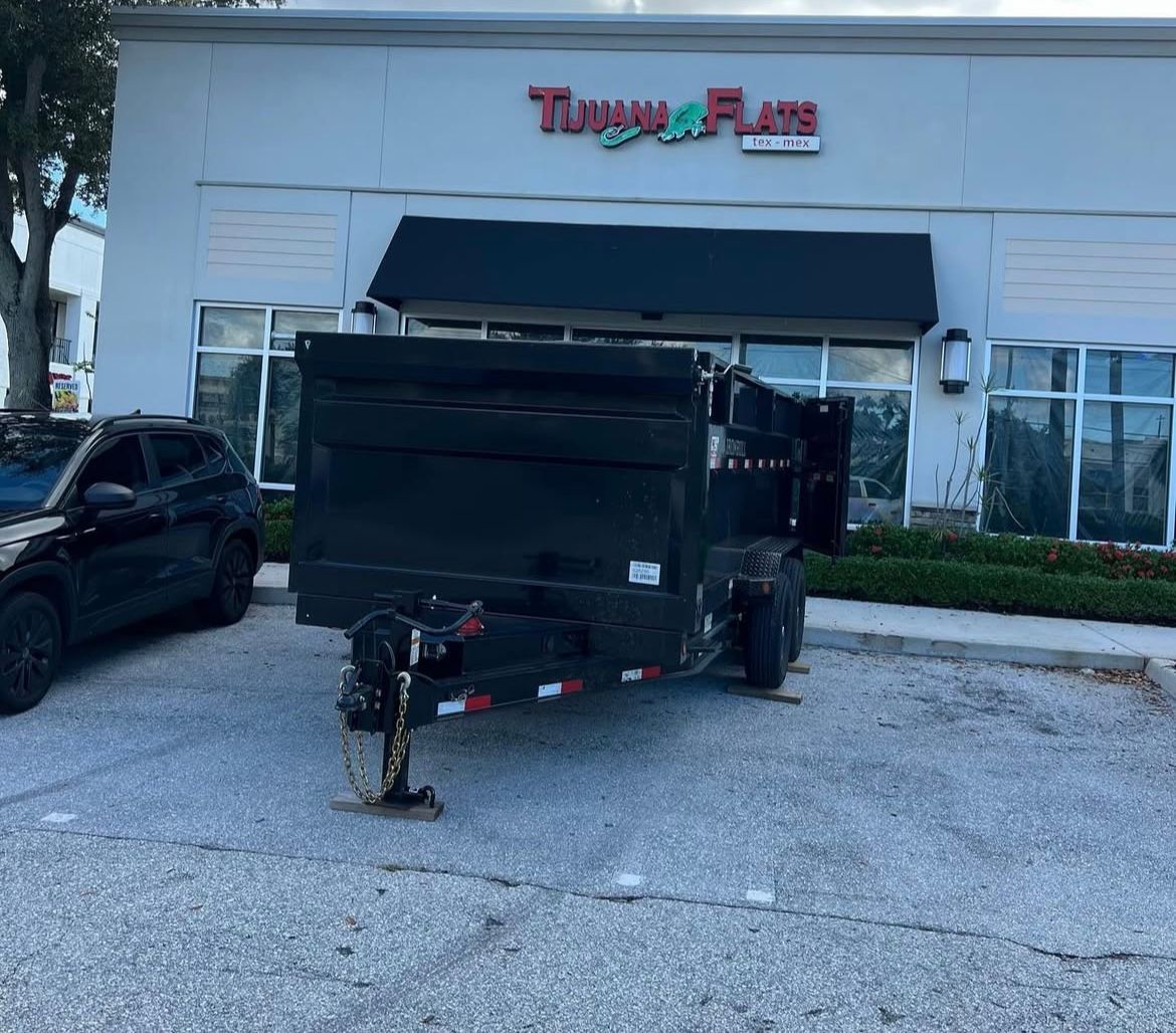 A black dump trailer parked in front of a Tijuana Flats restaurant on a sunny day.
