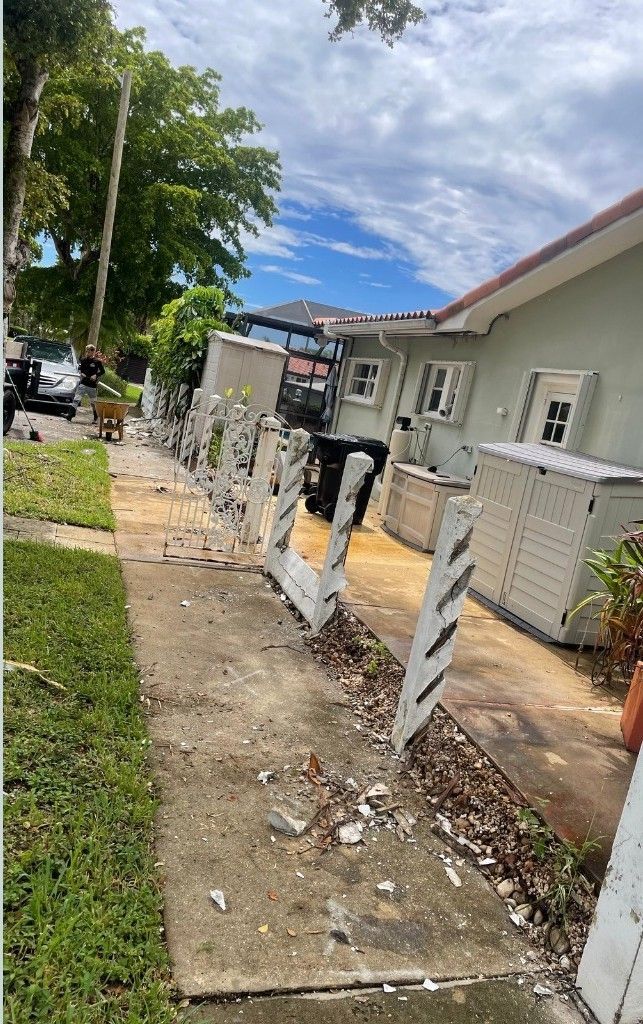 A row of white, angled fence posts standing in a grassy yard next to a paved walkway and a light-colored house.