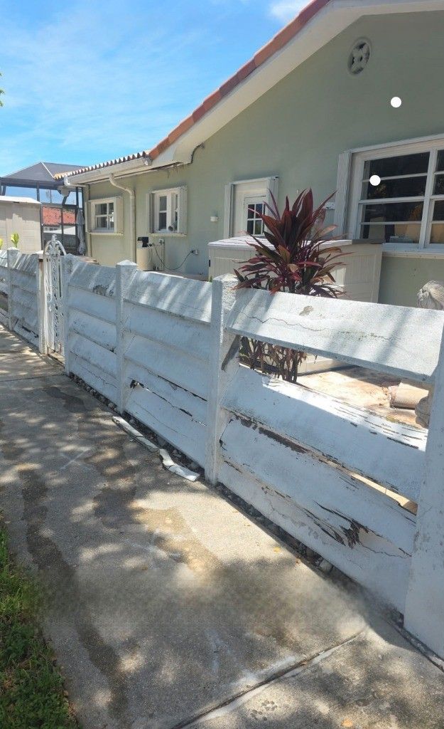 A light-colored house behind a white, tiered concrete fence on a sunny day.