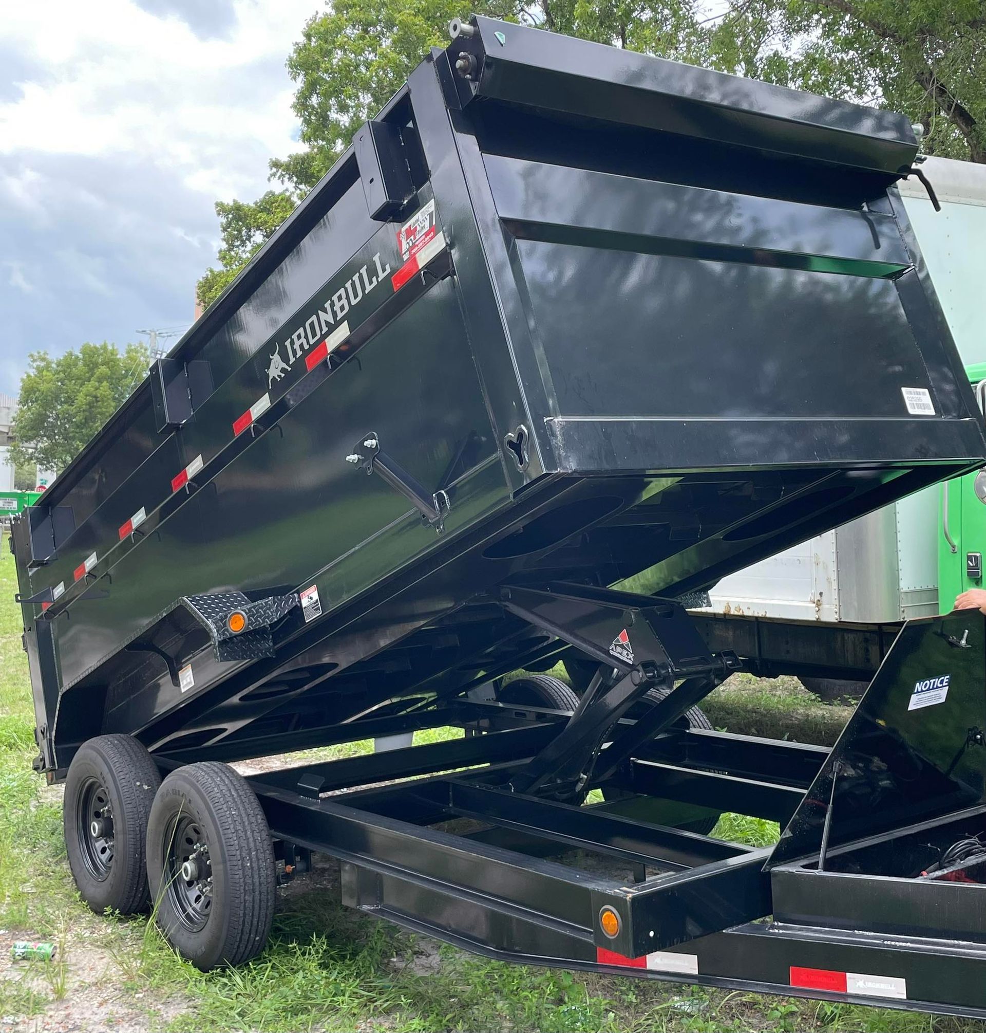 A black Iron Bull dump trailer in a raised, tilted position, parked outdoors on a grassy lot.