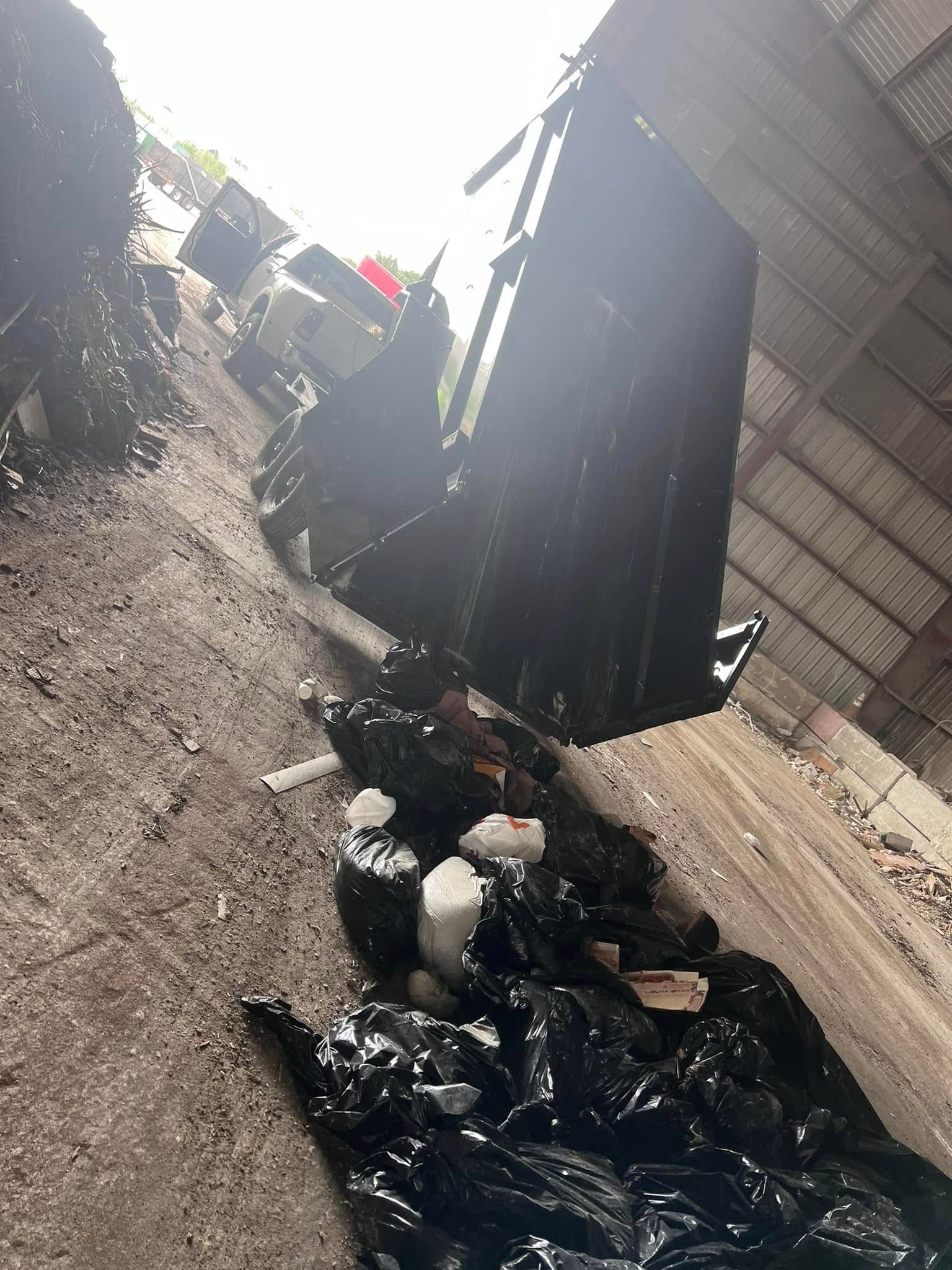 A metal industrial chute or container surrounded by black plastic debris on a dirt floor inside a warehouse.