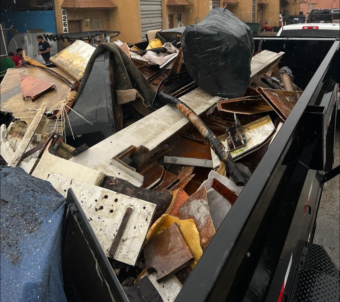 A full load of construction debris, wood scraps, and a black trash bag inside a black dump trailer.