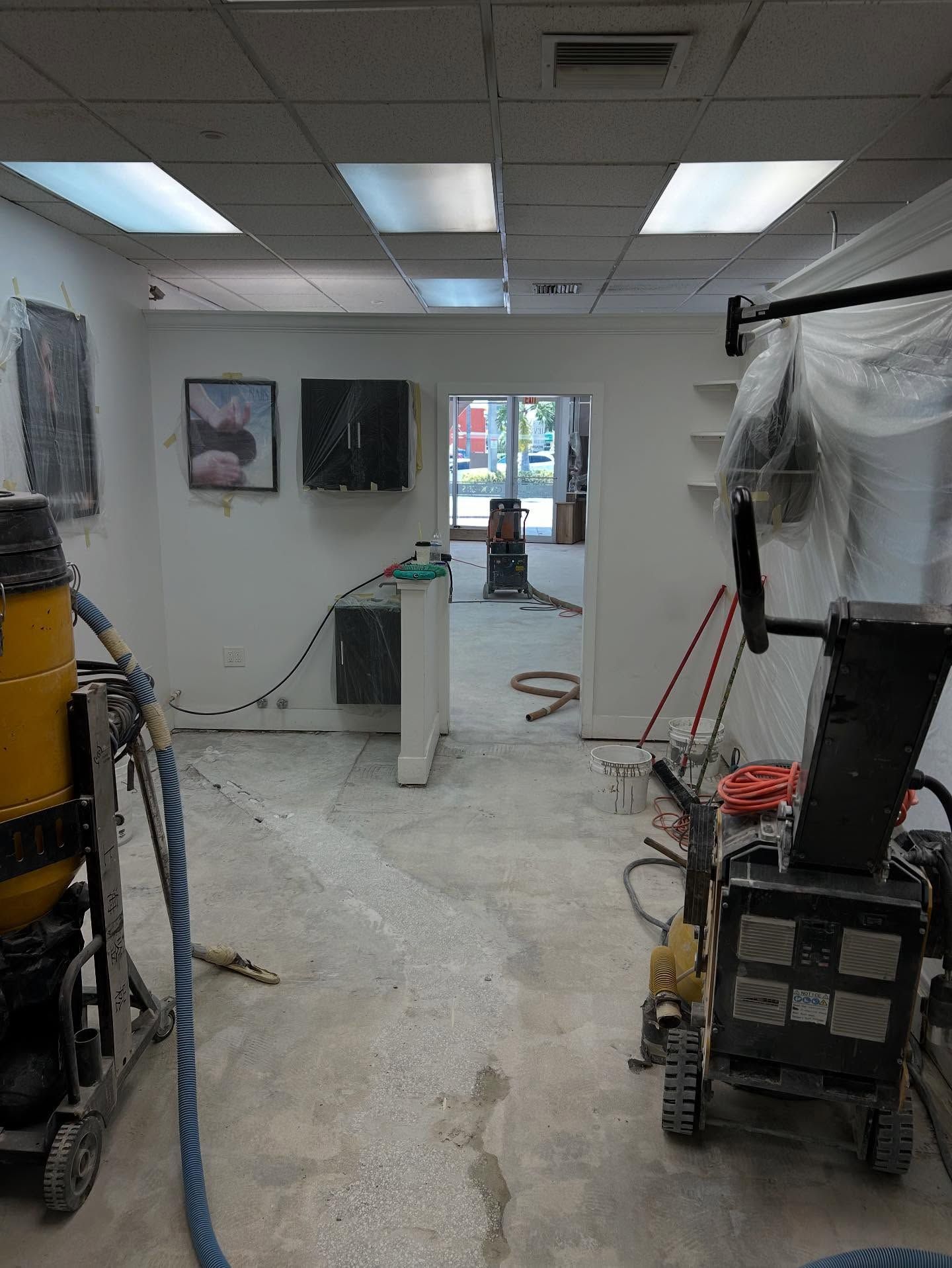 Interior of a room under renovation with concrete flooring, construction equipment, and white walls.