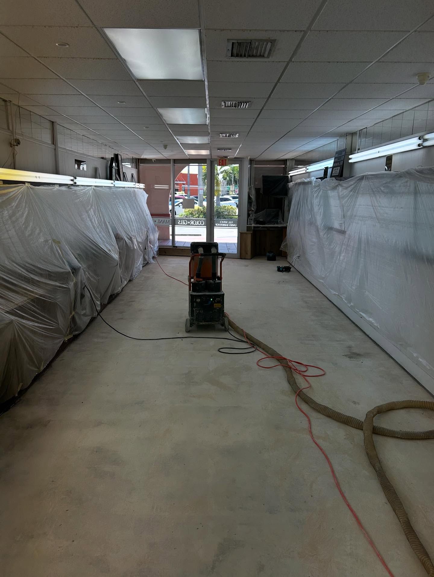 A commercial space under renovation, with furniture covered in plastic and a floor sander in the center.