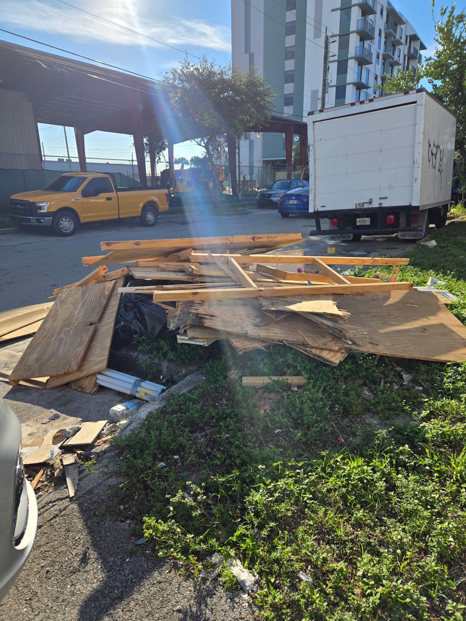 A pile of discarded wooden boards and construction debris sitting on the grass in a parking lot.