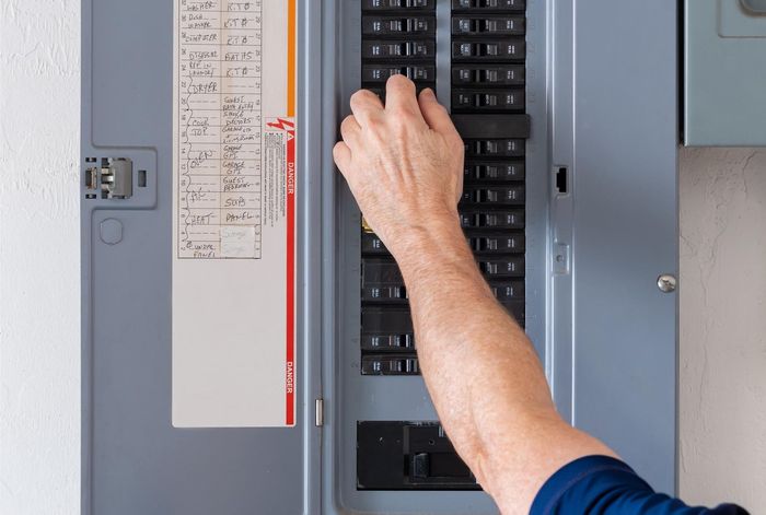 Hand turning on a circuit breaker in a gray electrical panel.