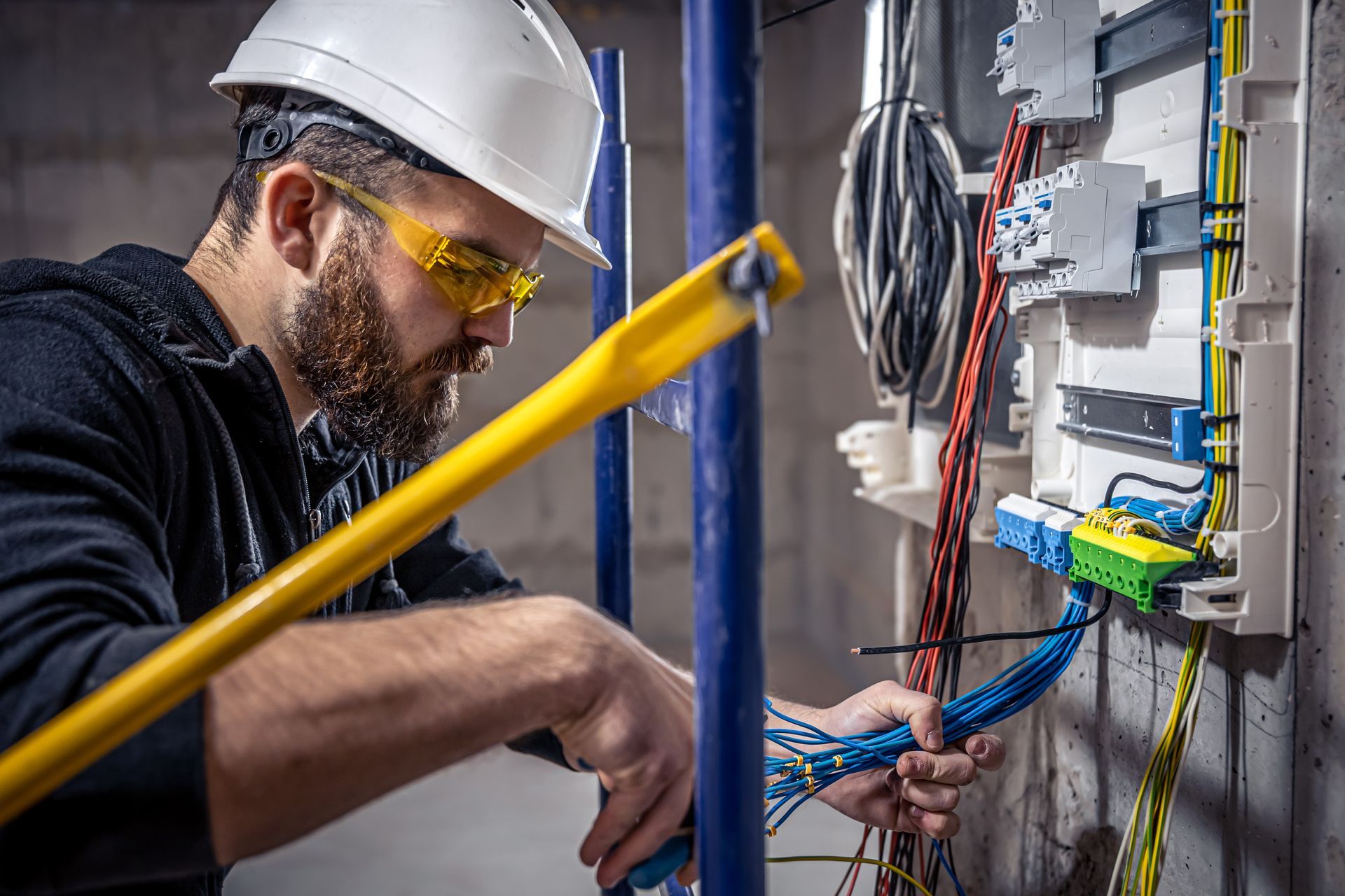 Electrician in safety gear works with wiring in a panel, indoors.