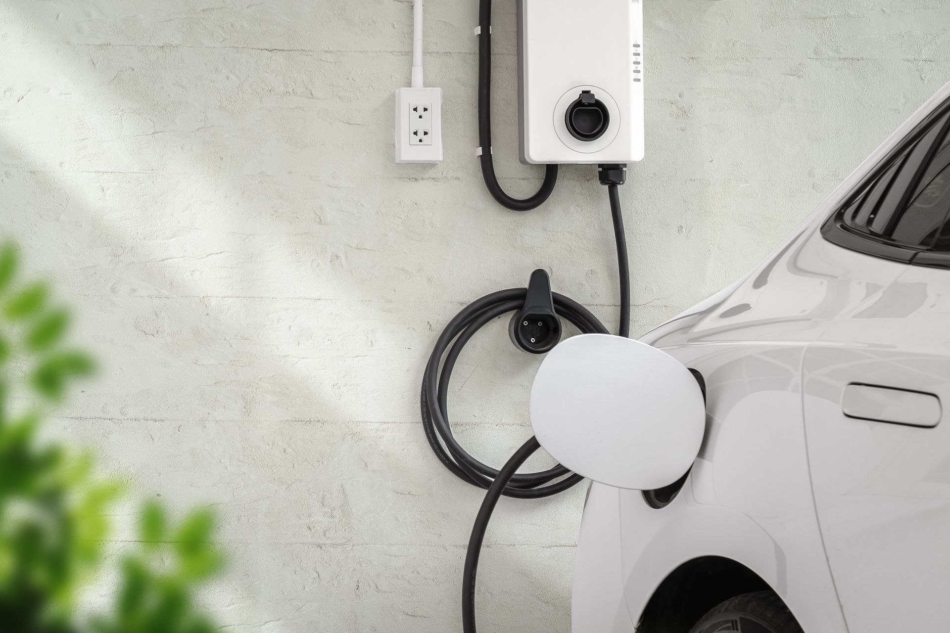 Electric vehicle charging beside a white car in a garage, with wall-mounted charger and coiled cable