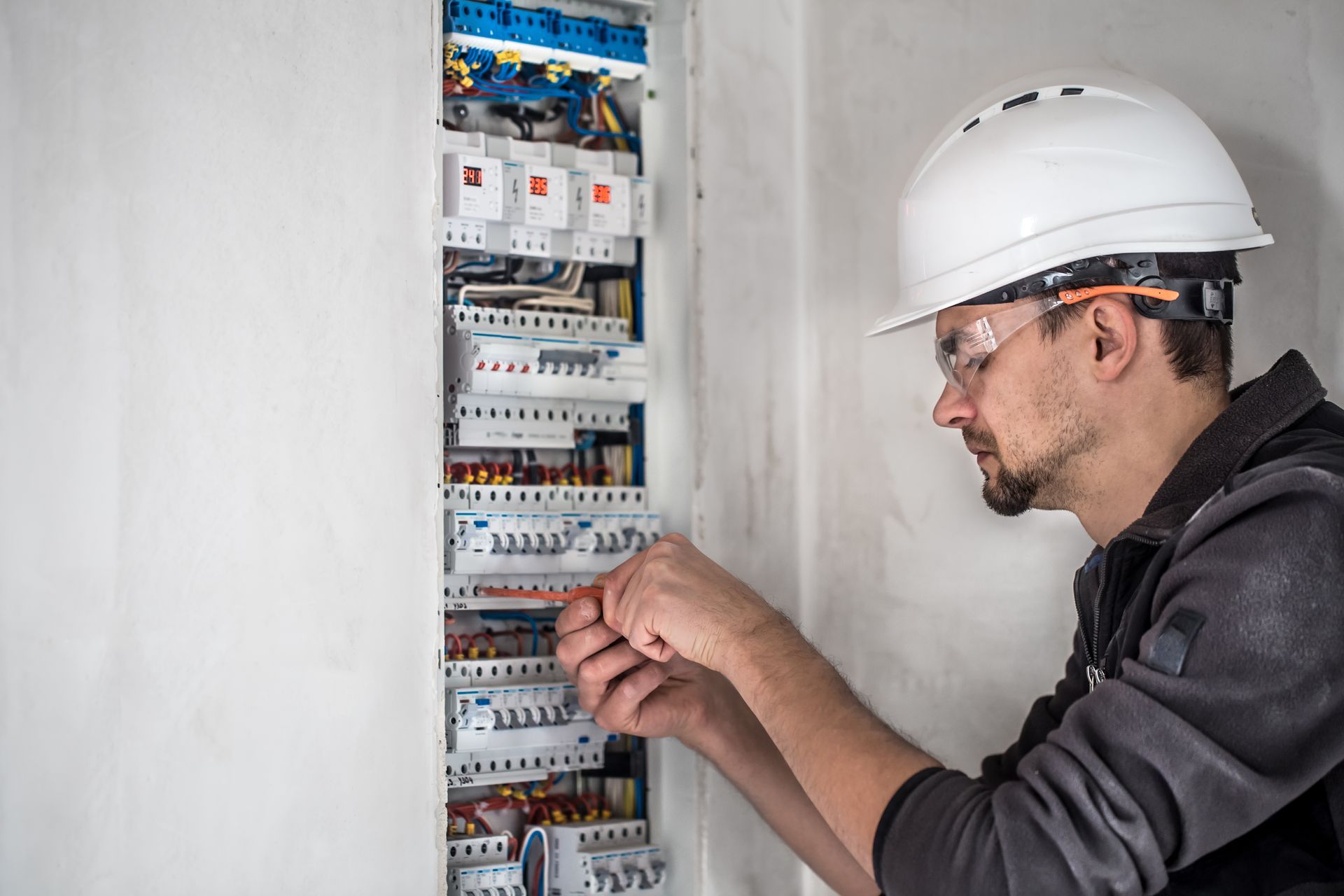 Electrician working on electrical panel, wearing safety glasses and hard hat.