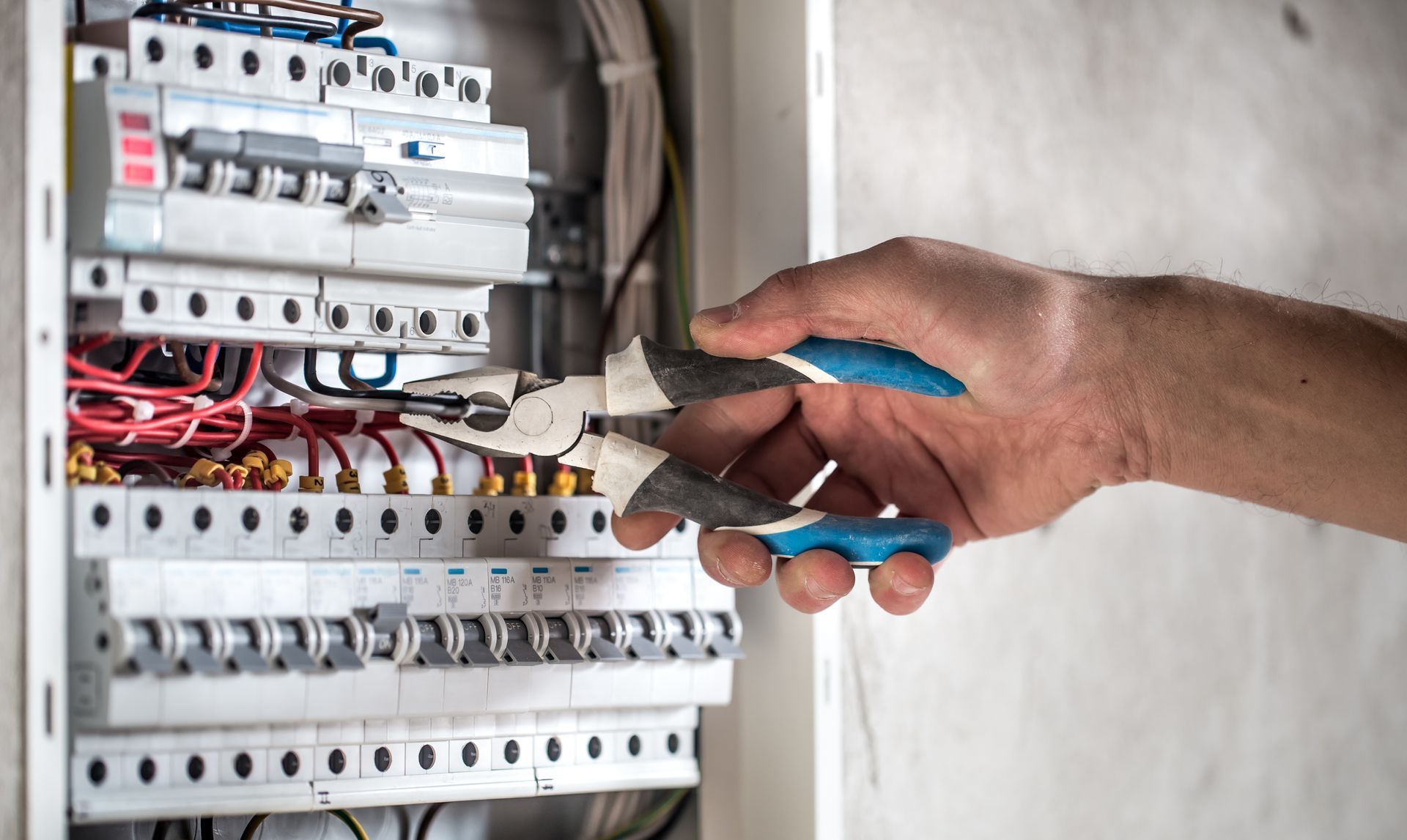 Hand using pliers on electrical panel. Wires and circuit breakers are visible.