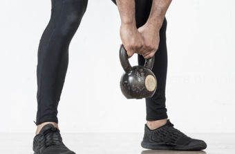 A person wearing black leggings and sneakers holds a kettlebell with both hands while in a bent-over position.