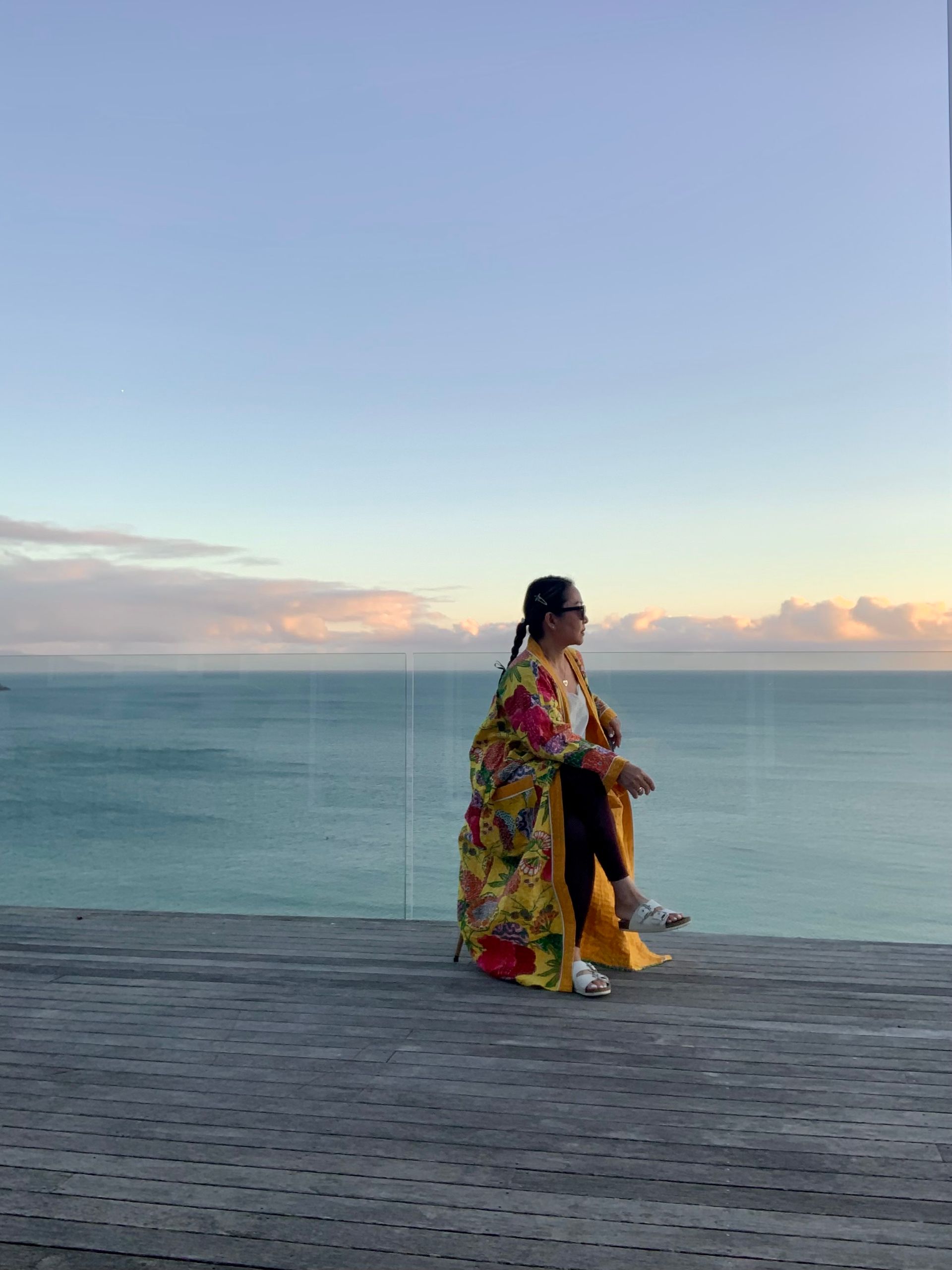 A woman is sitting on a pier overlooking the ocean.
