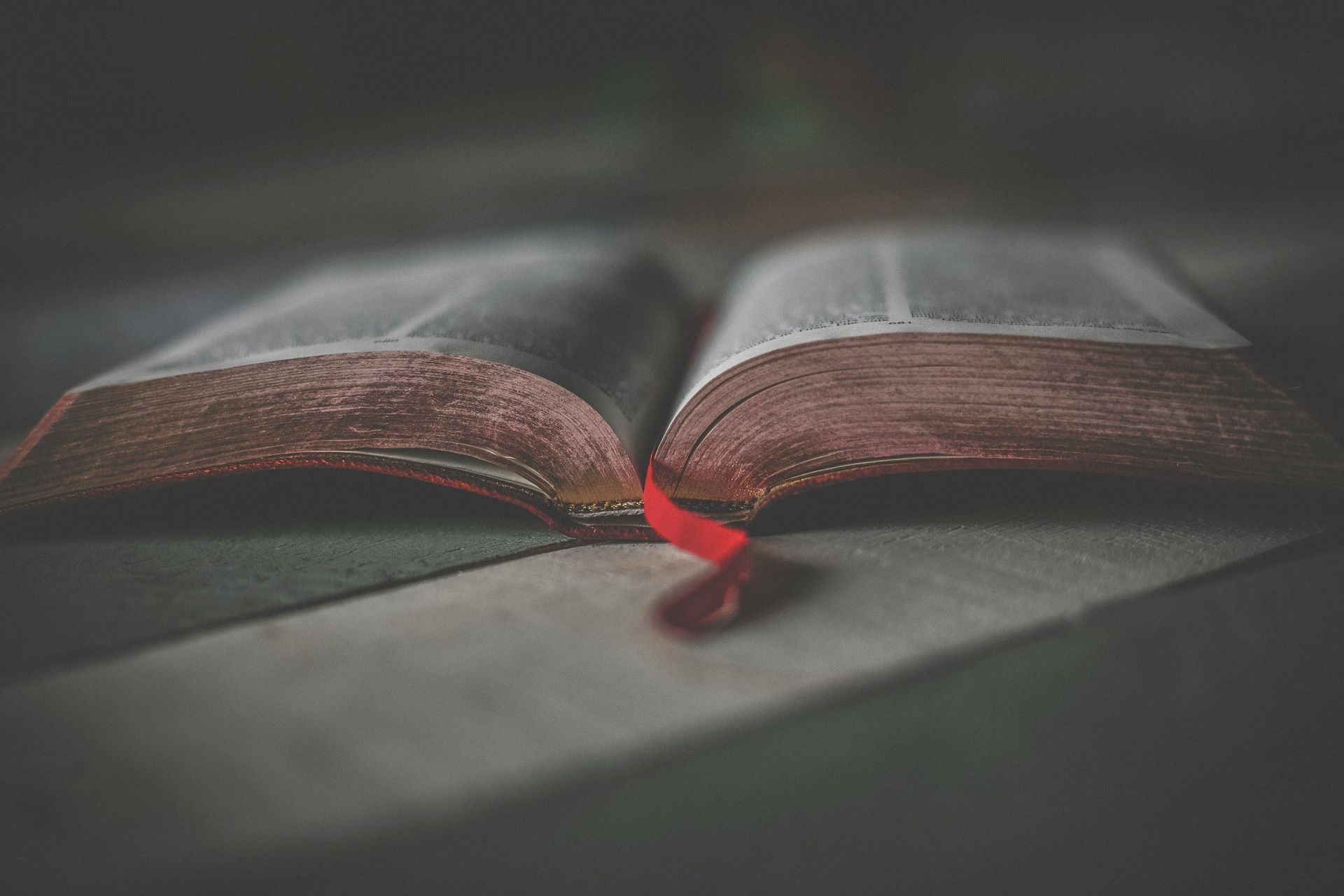 A close up of an ancient book with a red ribbon on a table.