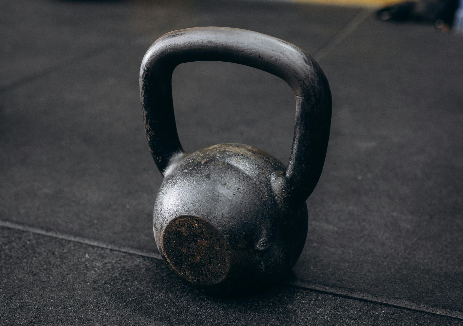 A black cast-iron kettlebell resting on a textured, dark rubber gym floor.