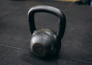 A black cast-iron kettlebell resting on a textured, dark rubber gym floor.