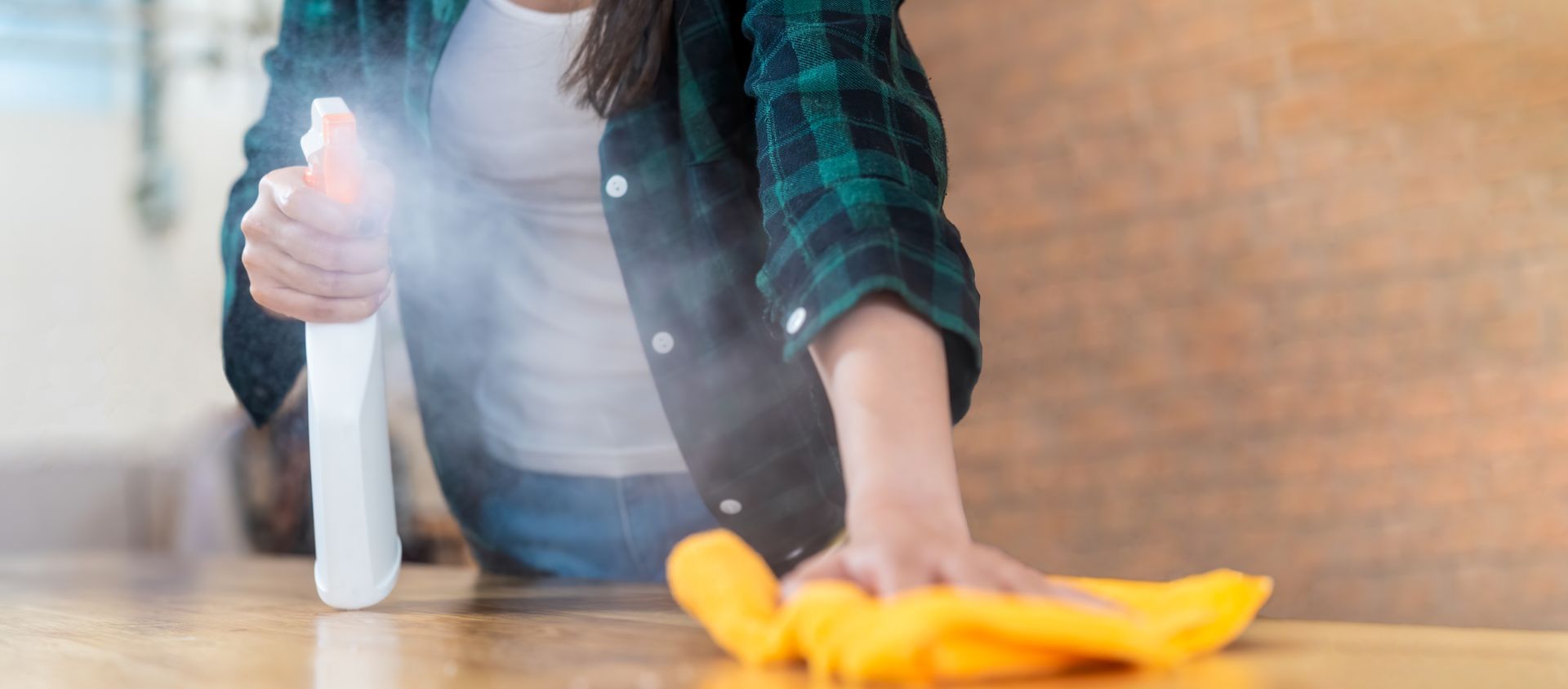 Person spraying cleaner and wiping a surface with a yellow cloth.