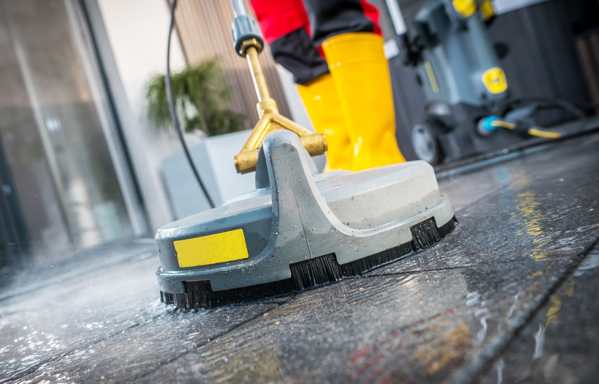Person in yellow boots using a power washer to clean a stone patio.