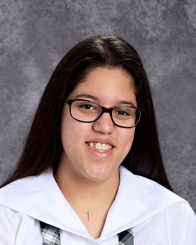 A girl wearing glasses and a cross necklace smiles for the camera