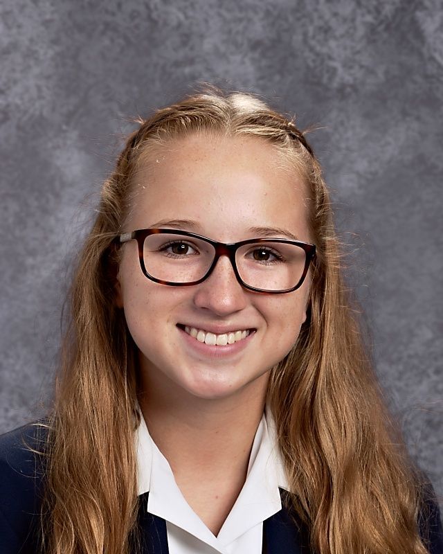 A young girl wearing glasses is smiling for the camera