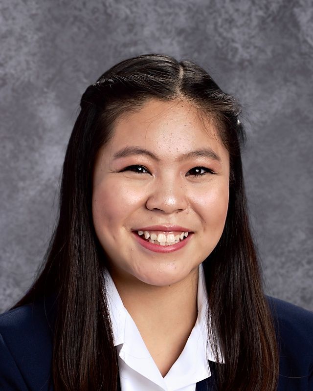 A young woman wearing a white shirt and a blue jacket is smiling for the camera.