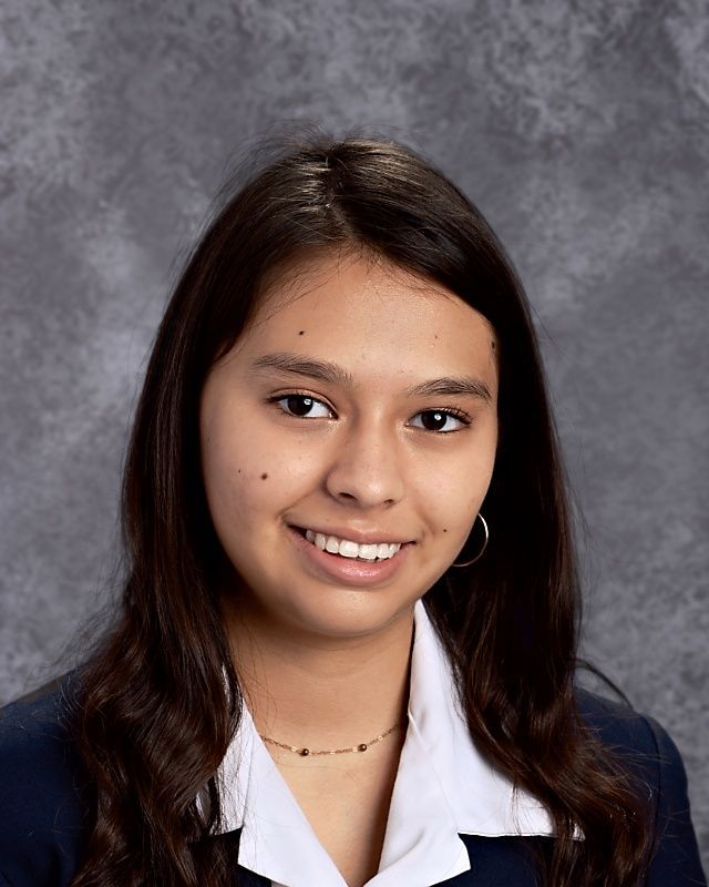 A young woman in a blue jacket and white shirt smiles for the camera