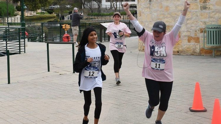 Three women wearing pink shirts are running in a park.