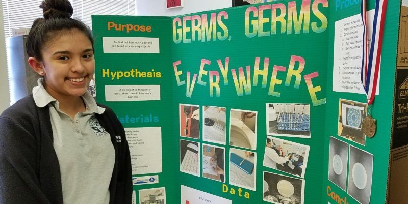 A girl is standing in front of a poster that says germs germs everywhere.