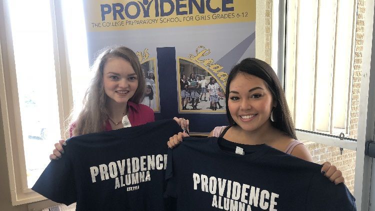 Two women are holding up t-shirts that say providence alumni