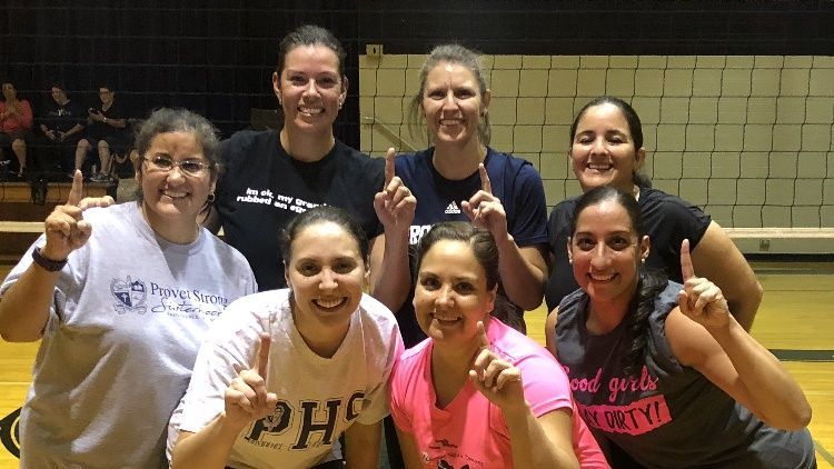 A group of women are posing for a picture in front of a volleyball net.