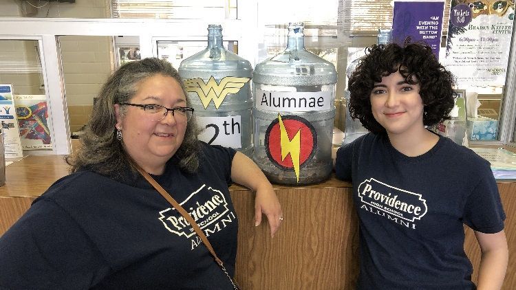 A woman and a girl are standing next to a water bottle that says ' alumni ' on it