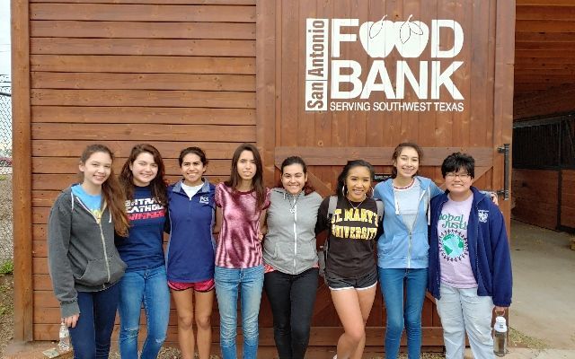 A group of young women are posing for a picture in front of a food bank.