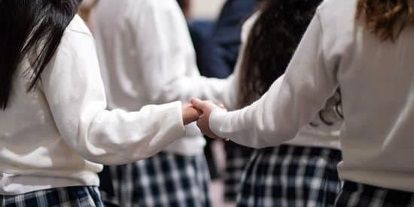 A group of girls in school uniforms are holding hands in a circle.